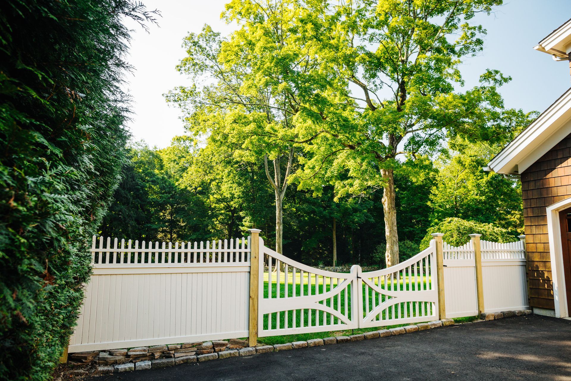 A white fence is surrounding a driveway leading to a house.