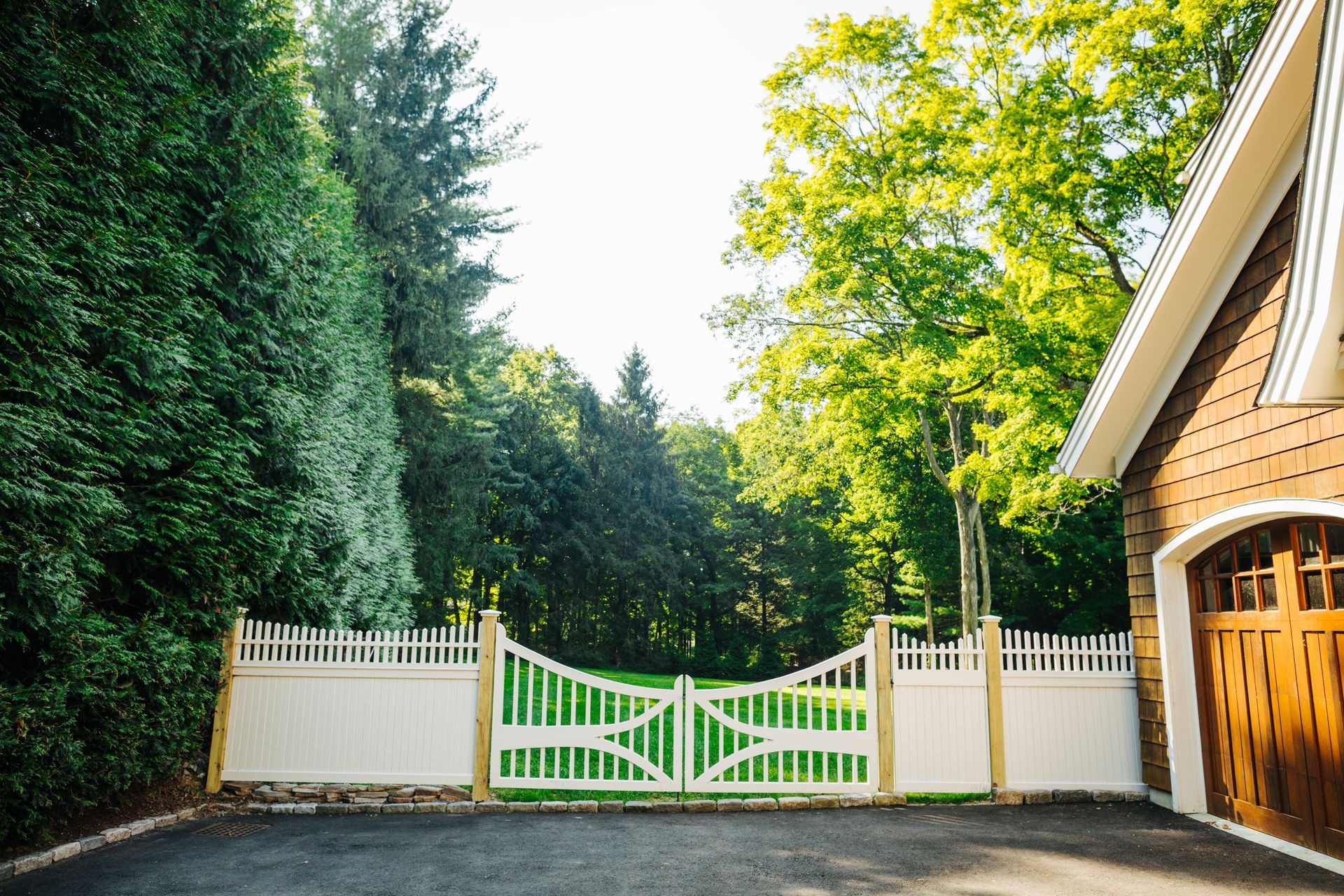 A driveway leading to a house with a white gate and a wooden garage door.