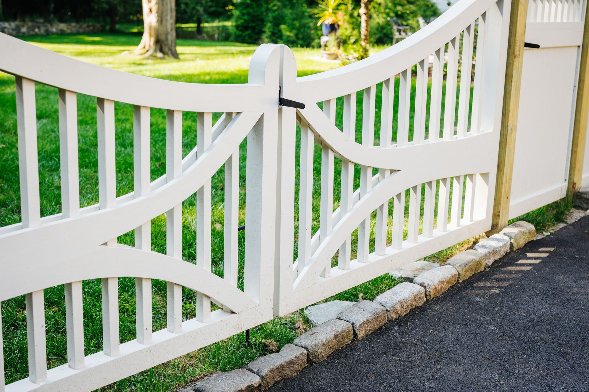 A white fence with a gate in the middle of a driveway.
