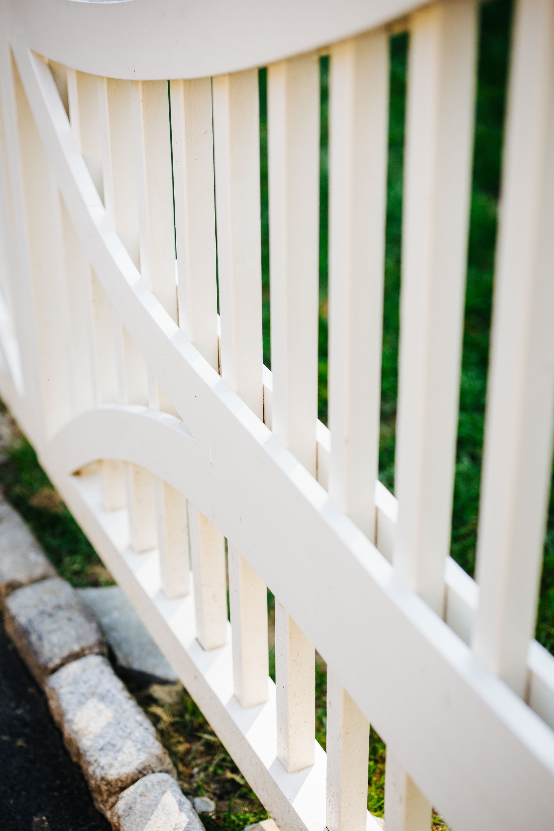 A close up of a white wooden fence with a green background.