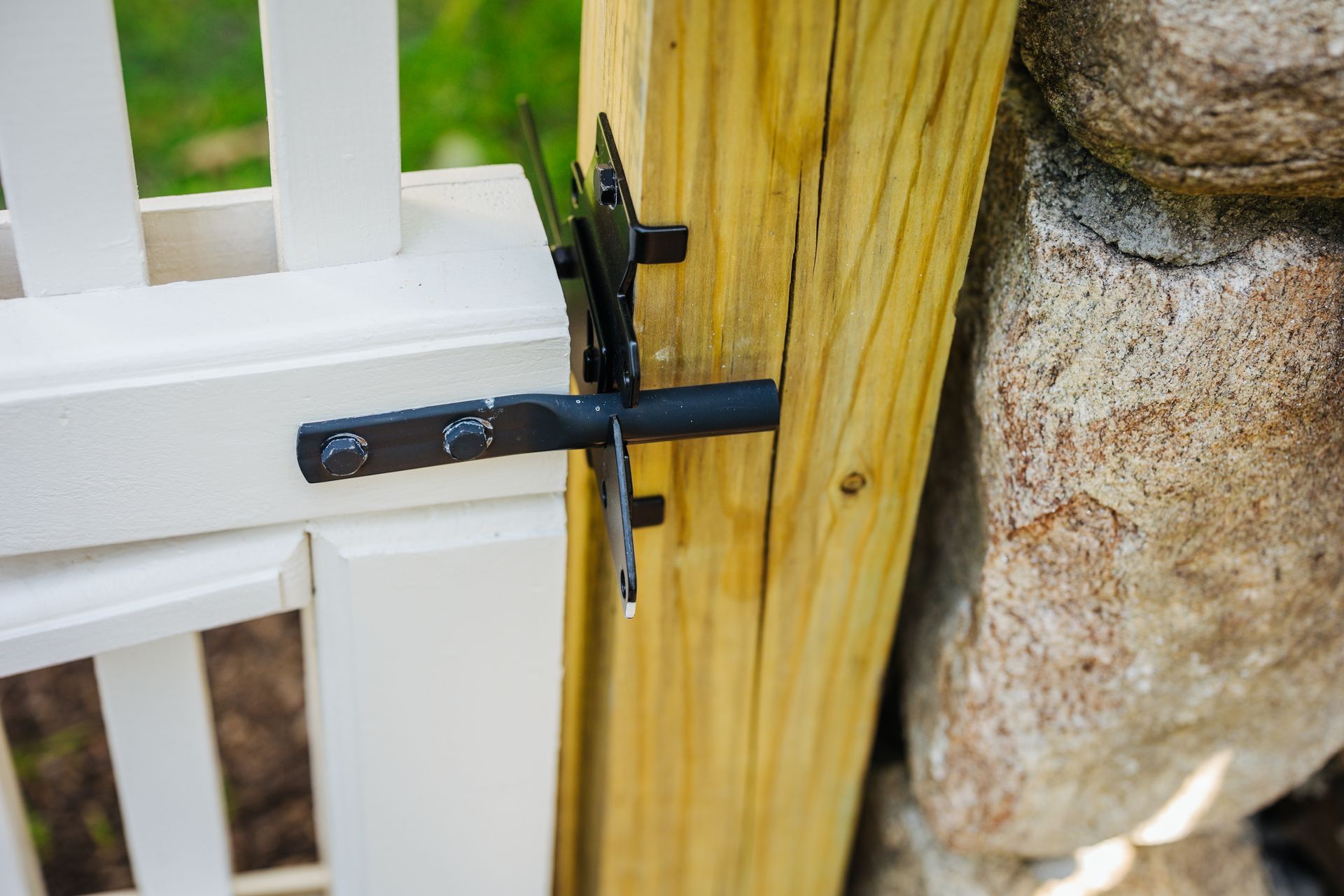 A white fence with a black latch is attached to a stone wall.