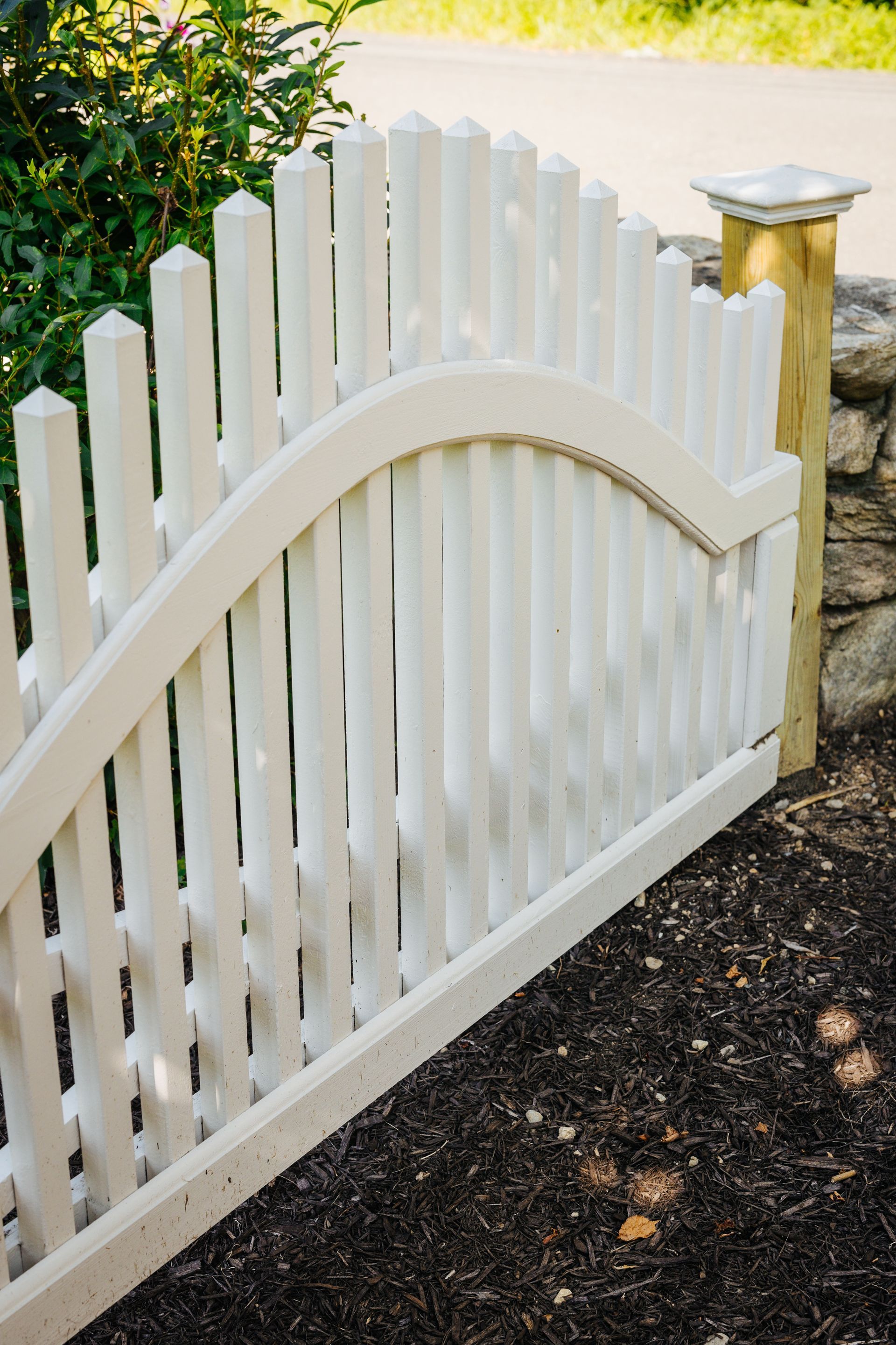 A white picket fence with a curved top is sitting next to a stone wall.