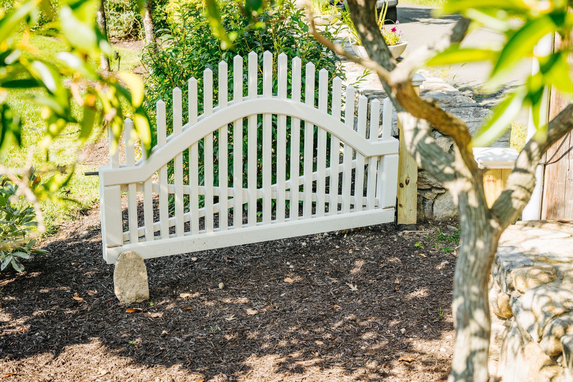 A white wooden bench is sitting under a tree in a garden.