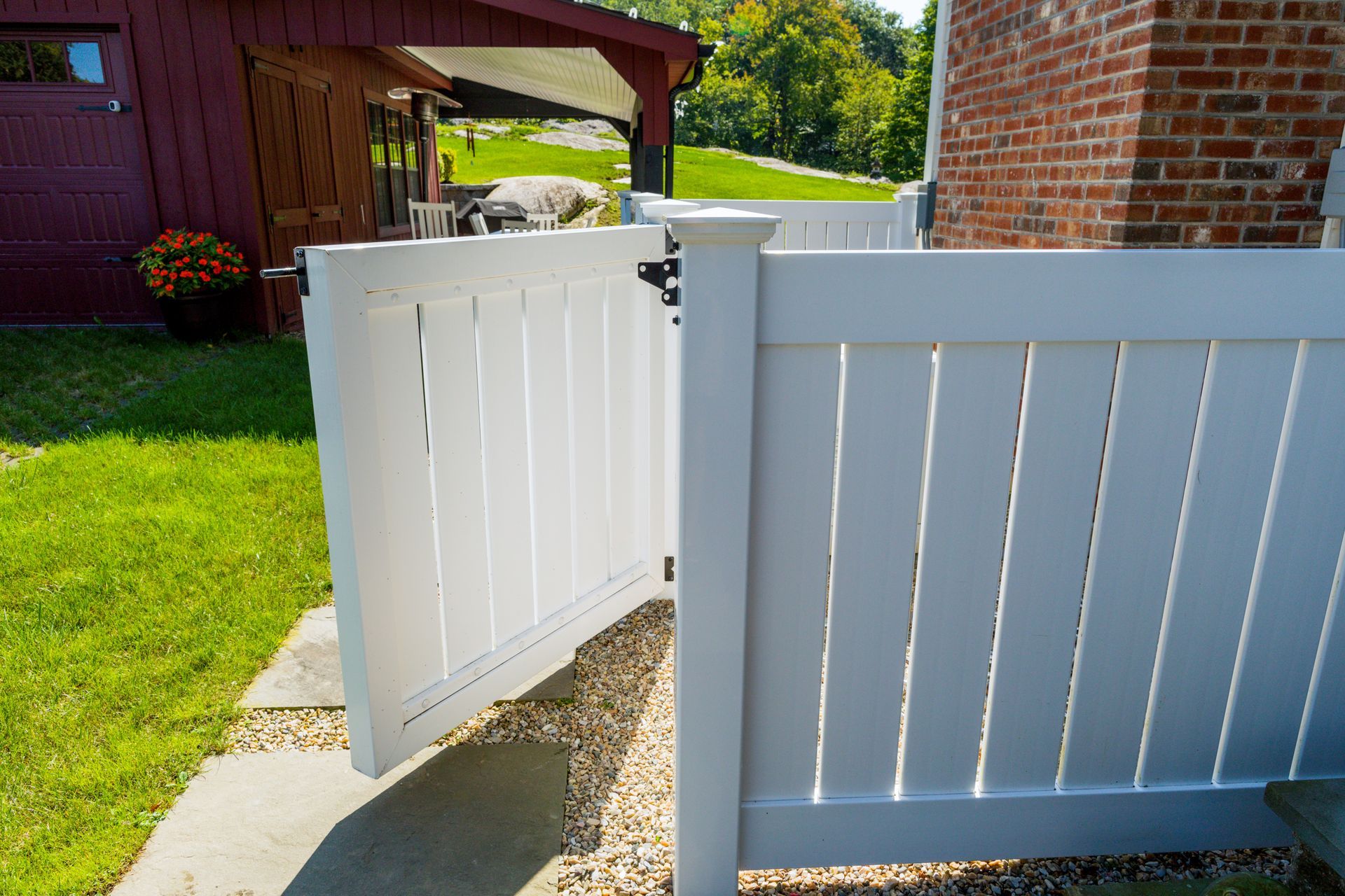 A white fence with a gate open in front of a brick building.