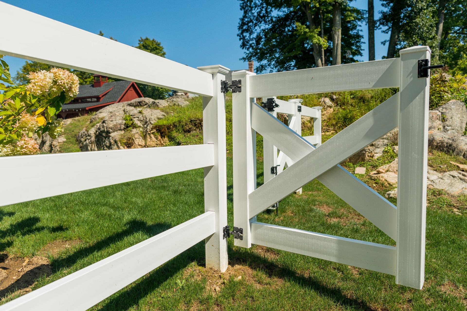 A white fence with a gate in the middle of a lush green field.