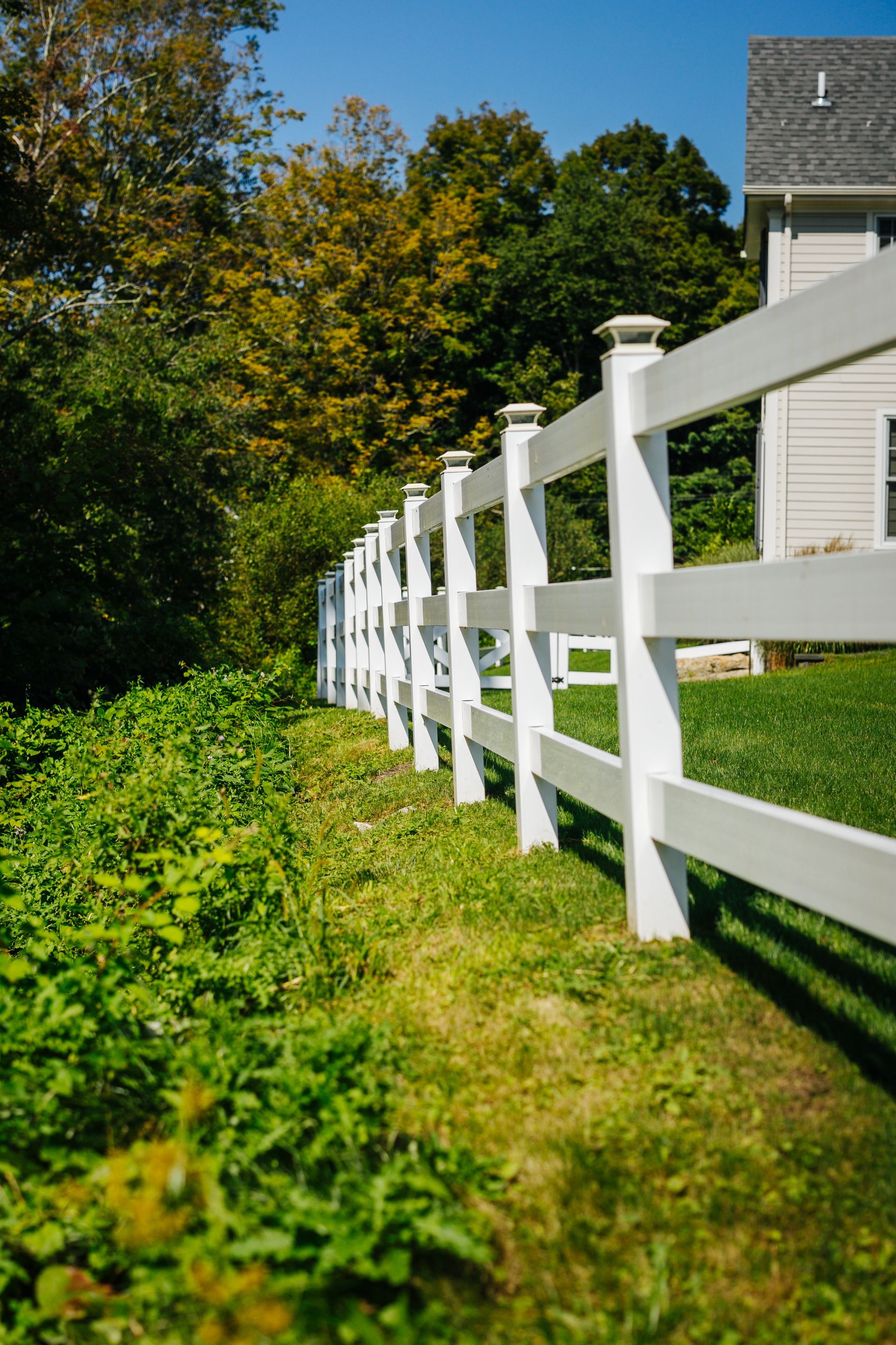 A white fence surrounds a lush green field in front of a house.