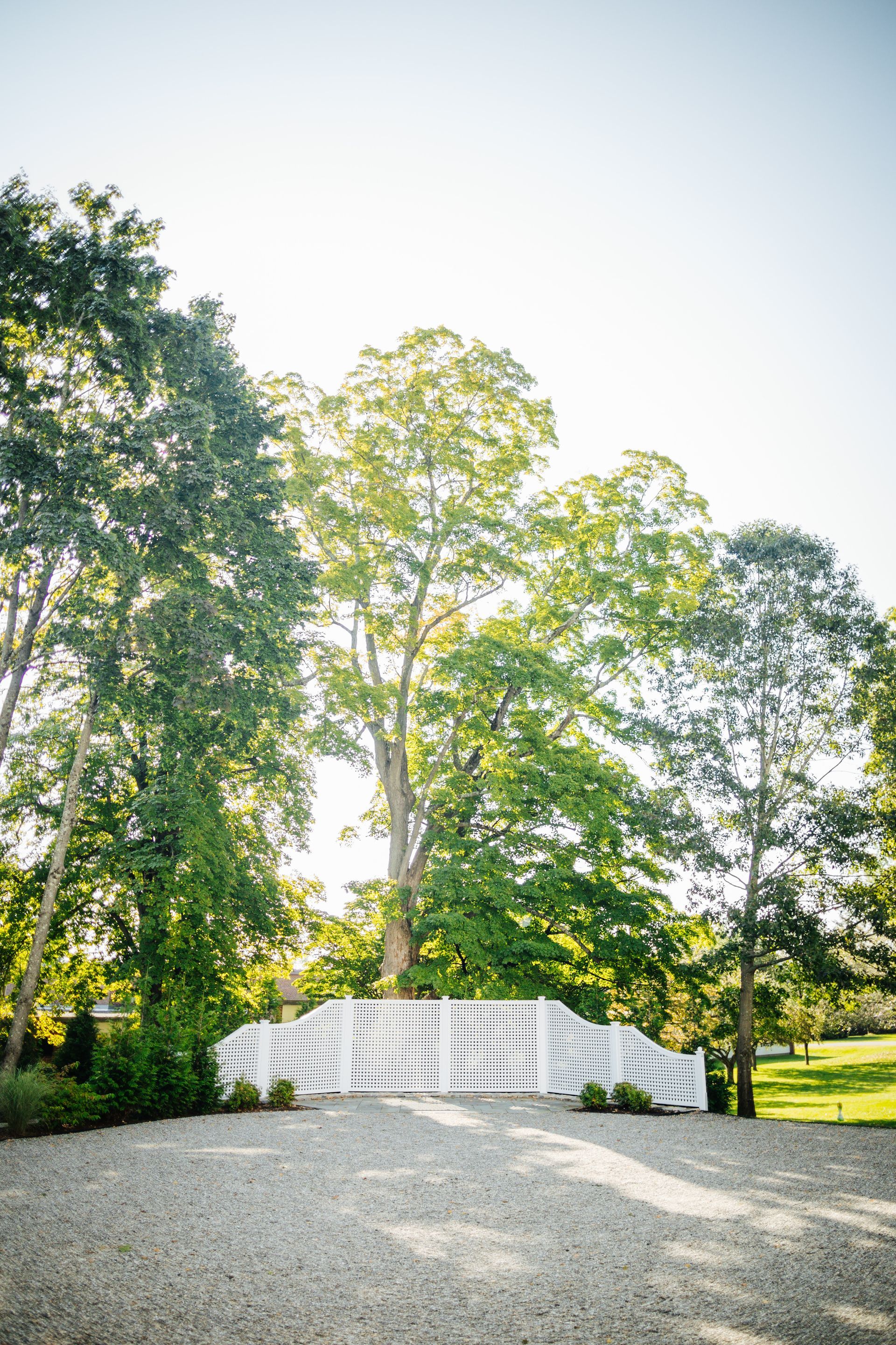 A white bridge is surrounded by trees on a gravel road.