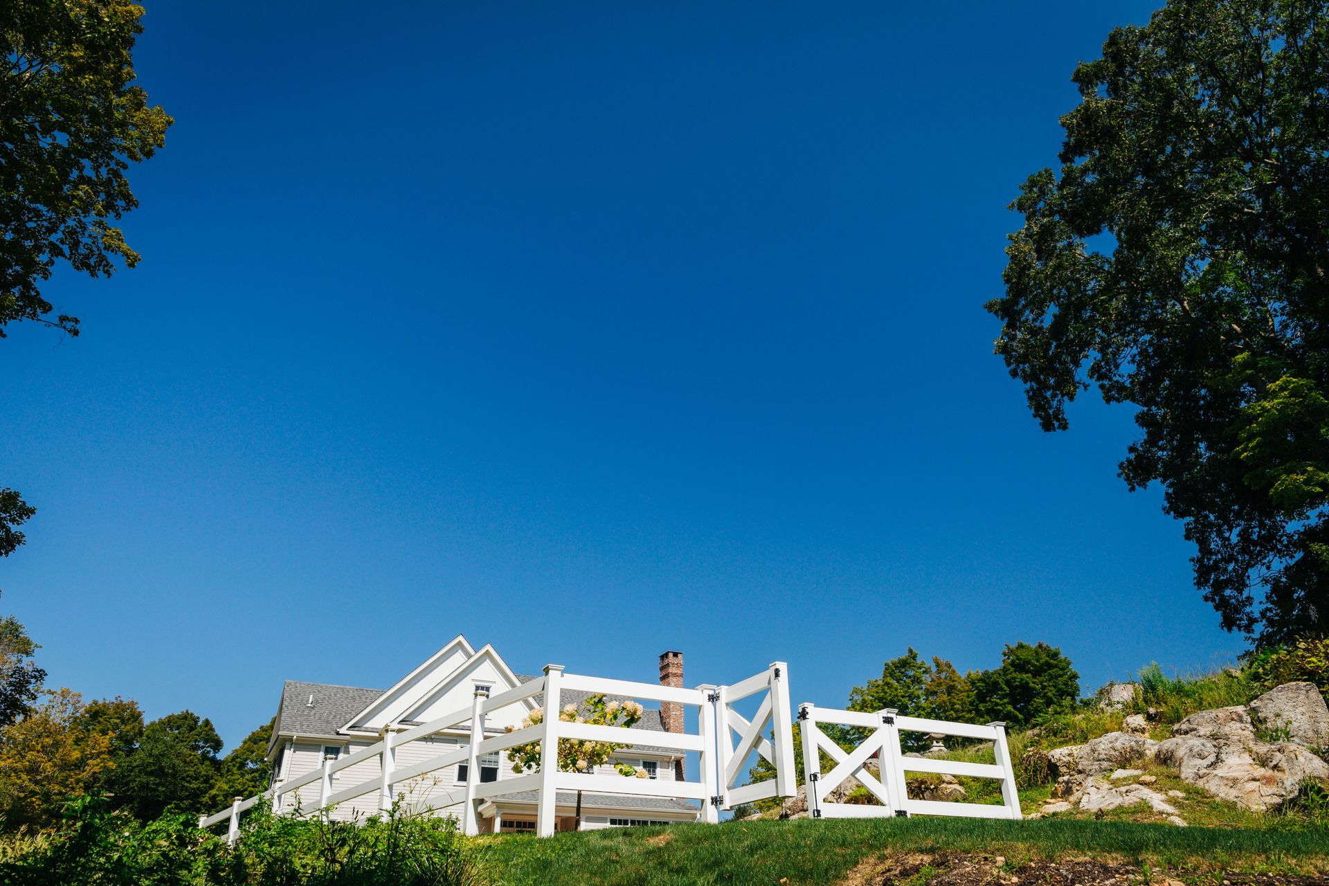 A white fence is surrounding a house on a hill.