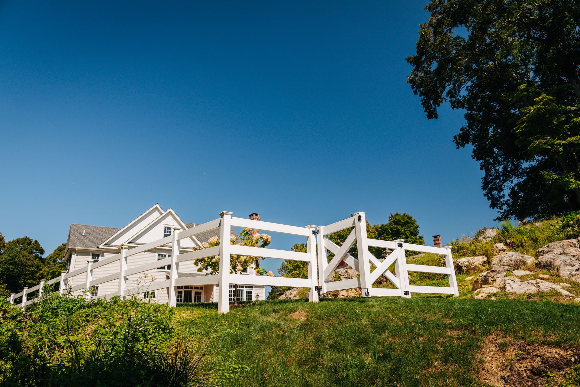 A white fence is sitting on top of a grassy hill in front of a house.