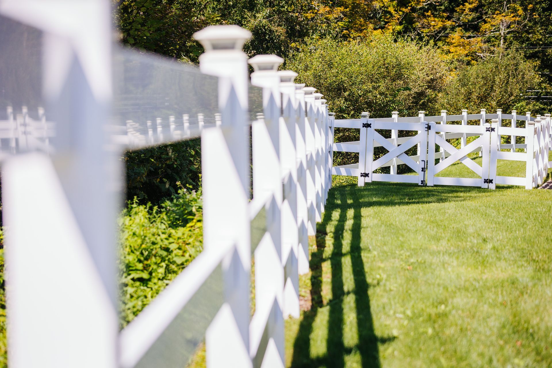 A white fence with a gate in the middle of a grassy field.
