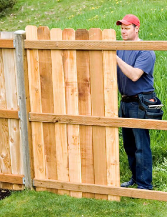 A man is standing next to a wooden fence.