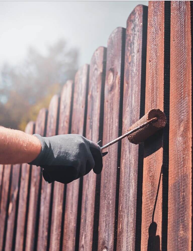 A person is painting a wooden fence with a roller.