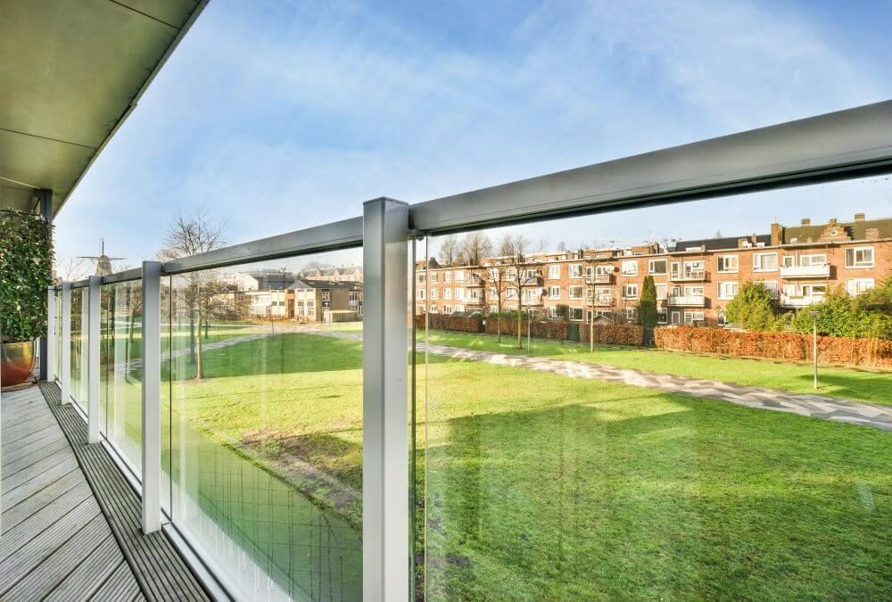 A balcony with a glass railing and a view of a park.