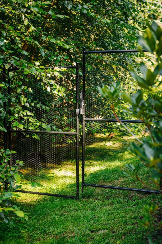 A black gate is open to a grassy area surrounded by trees.