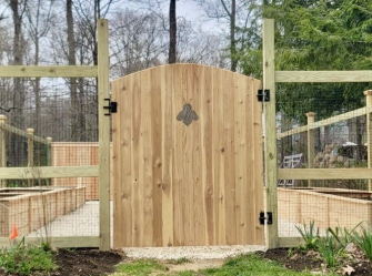 A wooden gate with a bee on it is surrounded by a wooden fence.