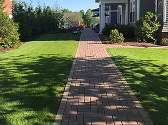 A brick walkway leading to a house with a lush green lawn.