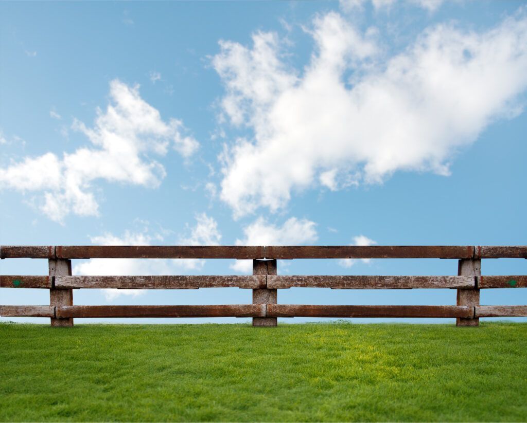 A wooden fence surrounds a grassy hill with a blue sky in the background