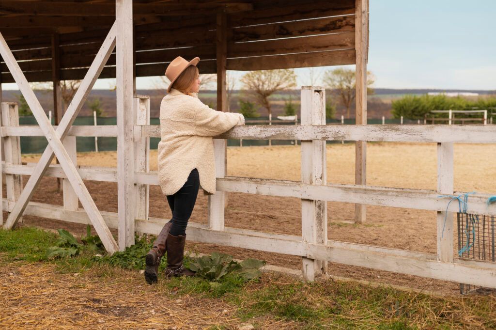 A woman in a cowboy hat is leaning on a wooden fence.