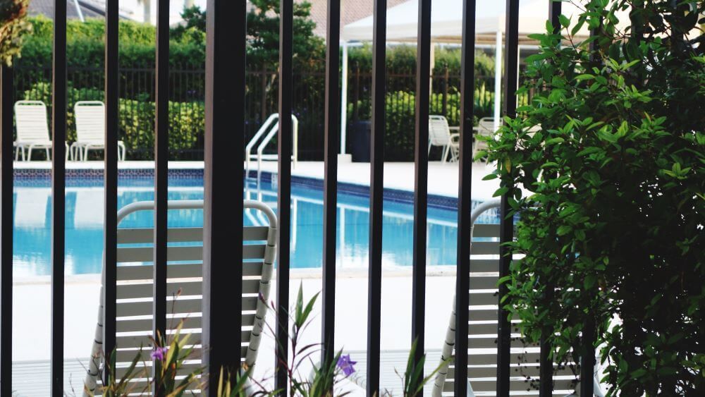 A view of a swimming pool through a metal fence.