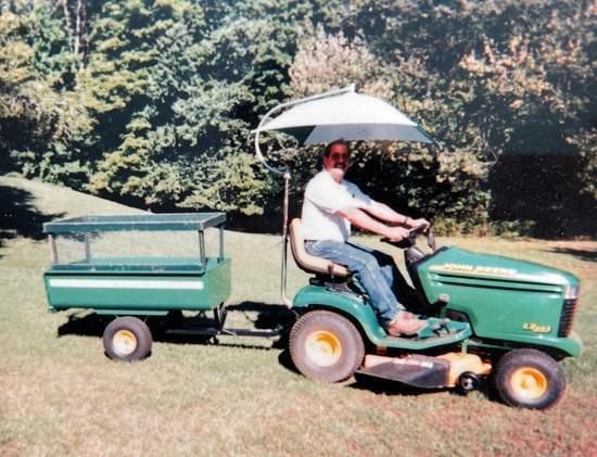 A man is riding a lawn mower with a trailer attached to it