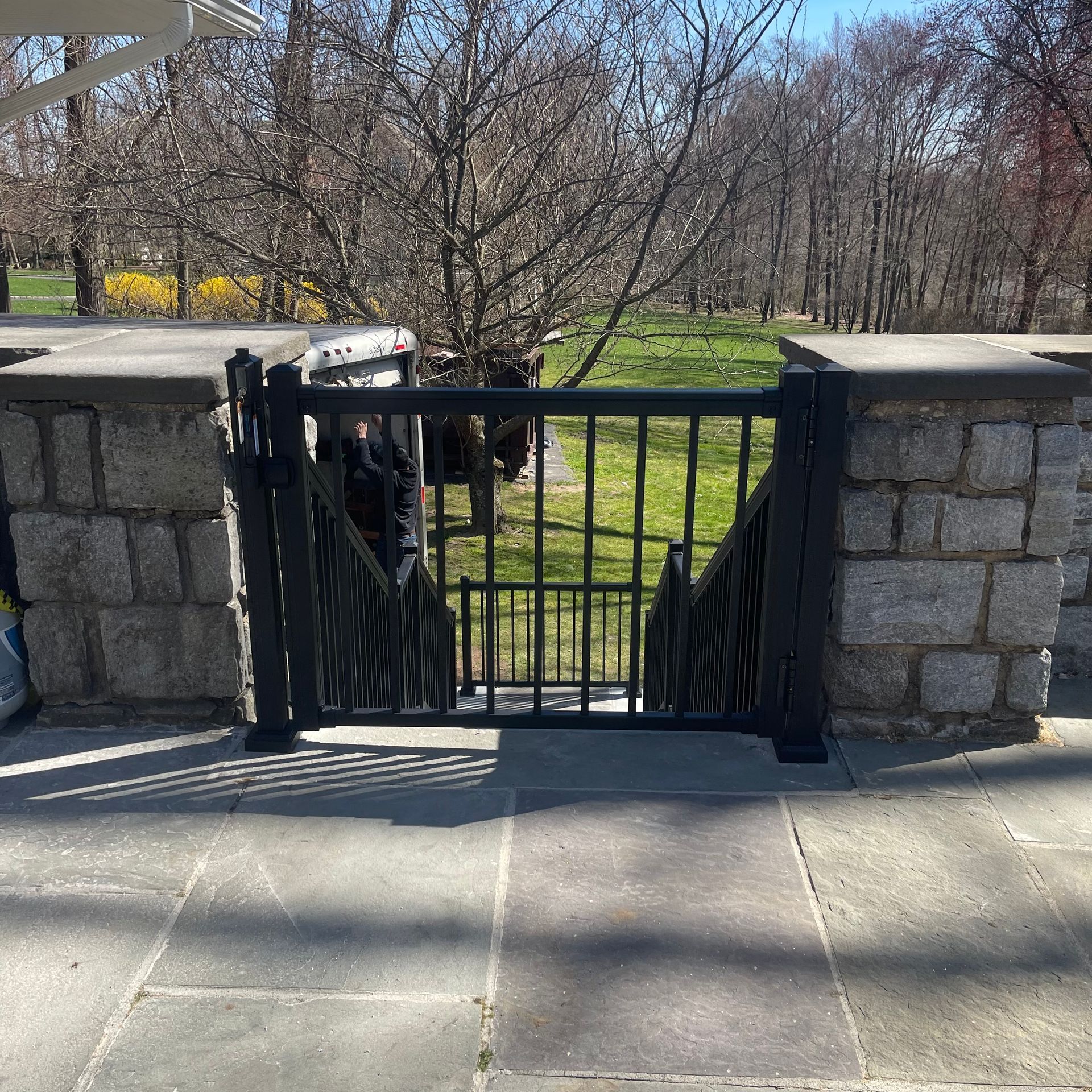 A black gate is sitting on a sidewalk next to a stone wall.