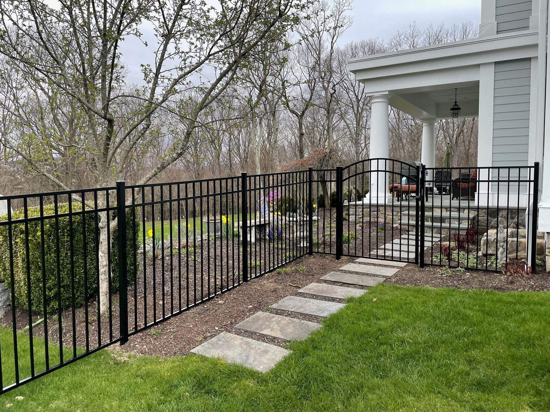 A black wrought iron fence surrounds a lush green yard in front of a white house.