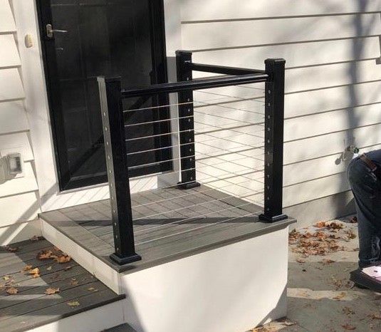 A person is sitting on the steps of a house with a black railing.