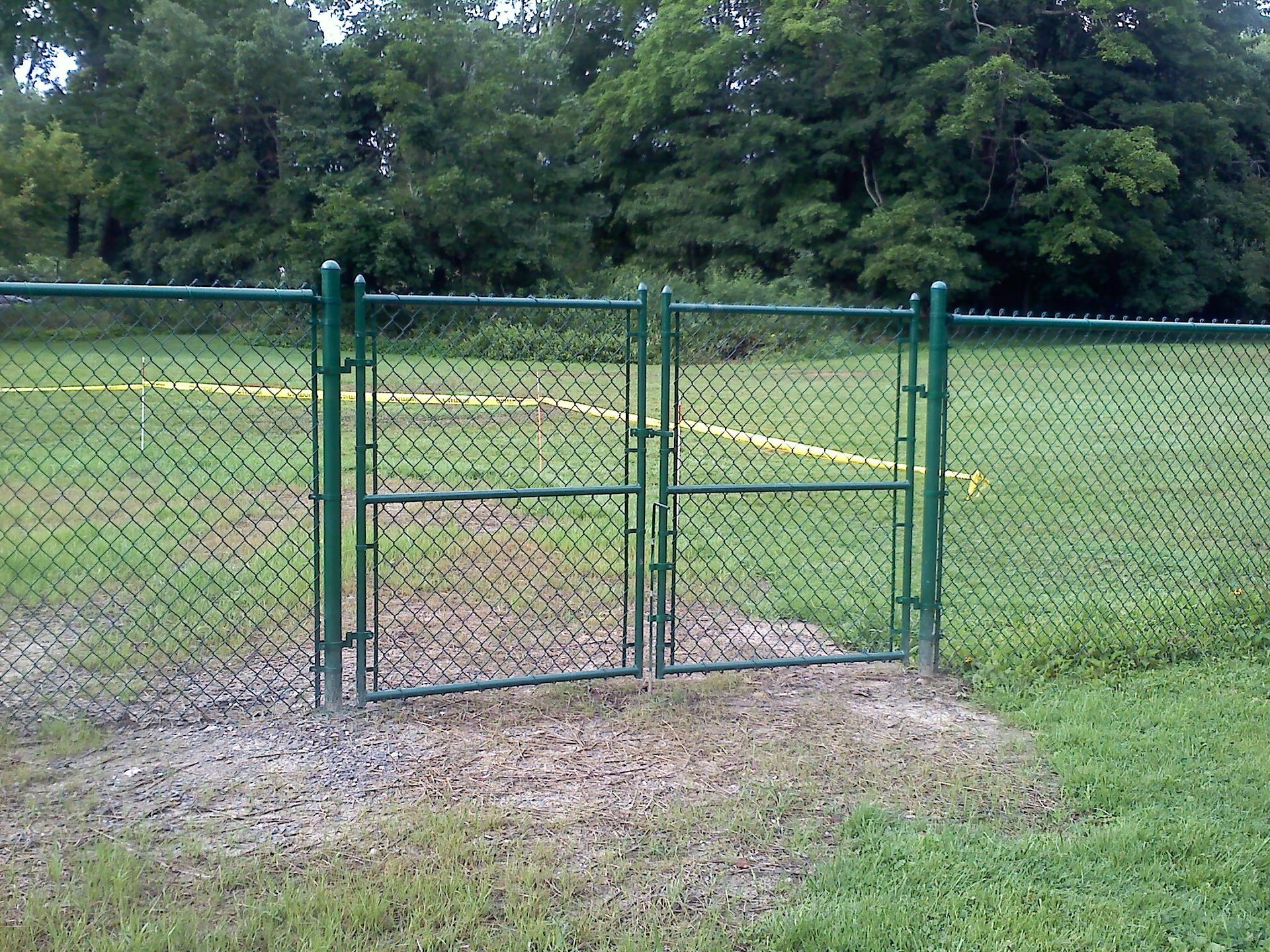 A green chain link fence with a gate in the grass