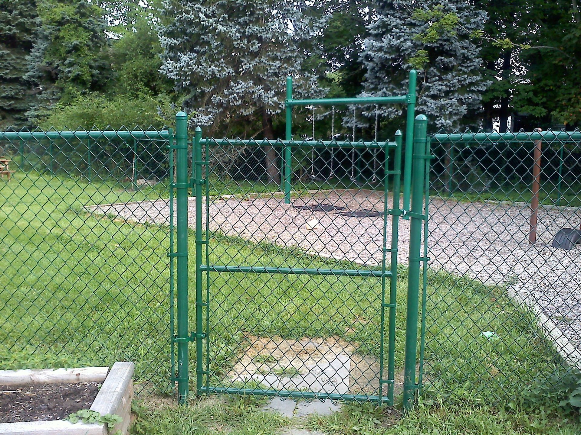A green chain link fence with a gate in the grass