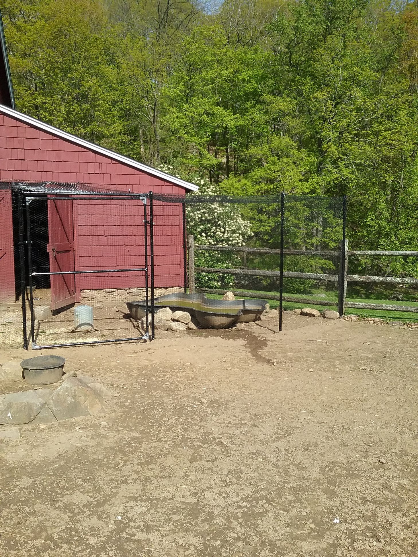 A red barn with a fence in front of it is surrounded by trees.