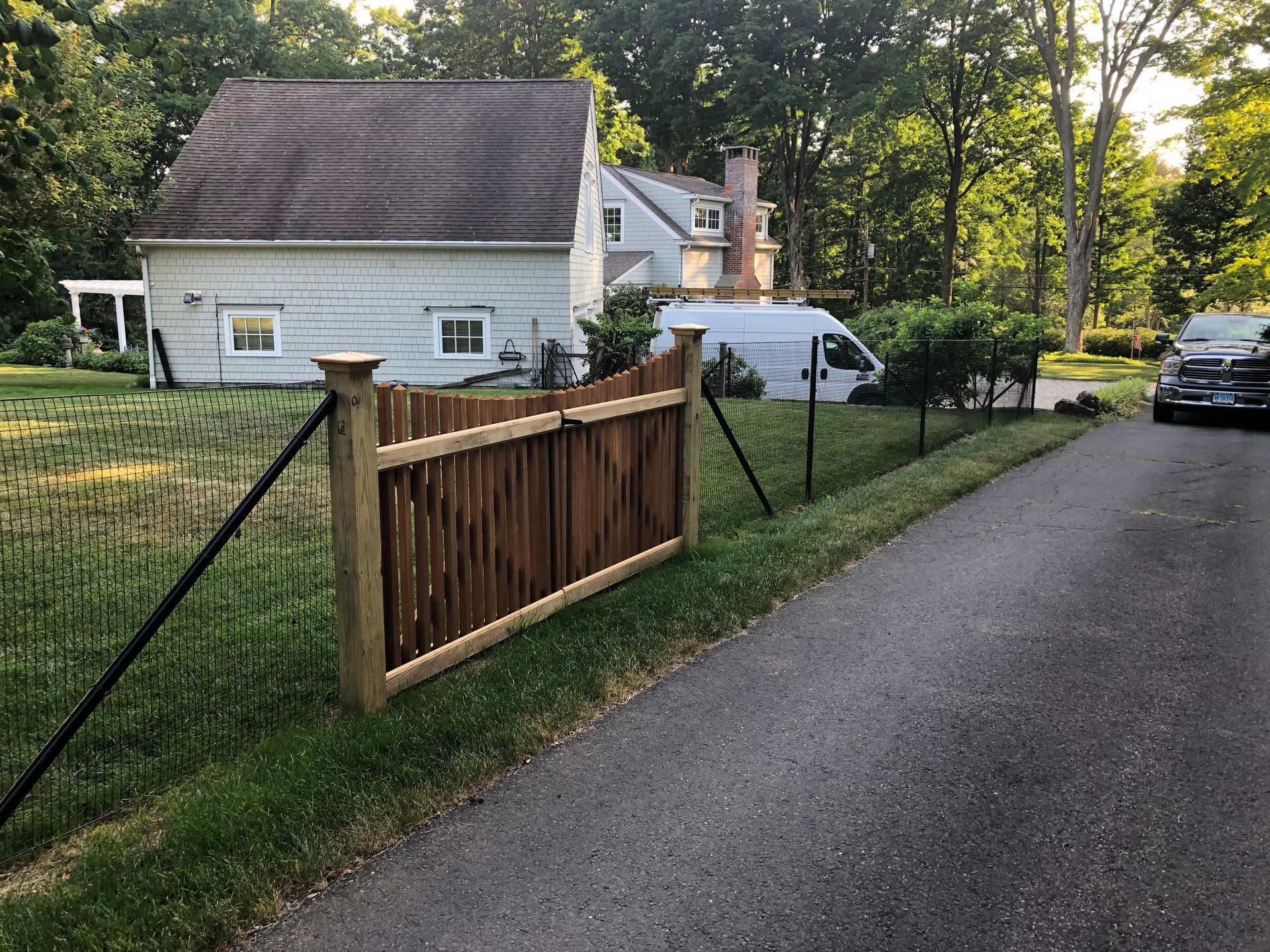 A wooden fence is along the side of a road in front of a house.
