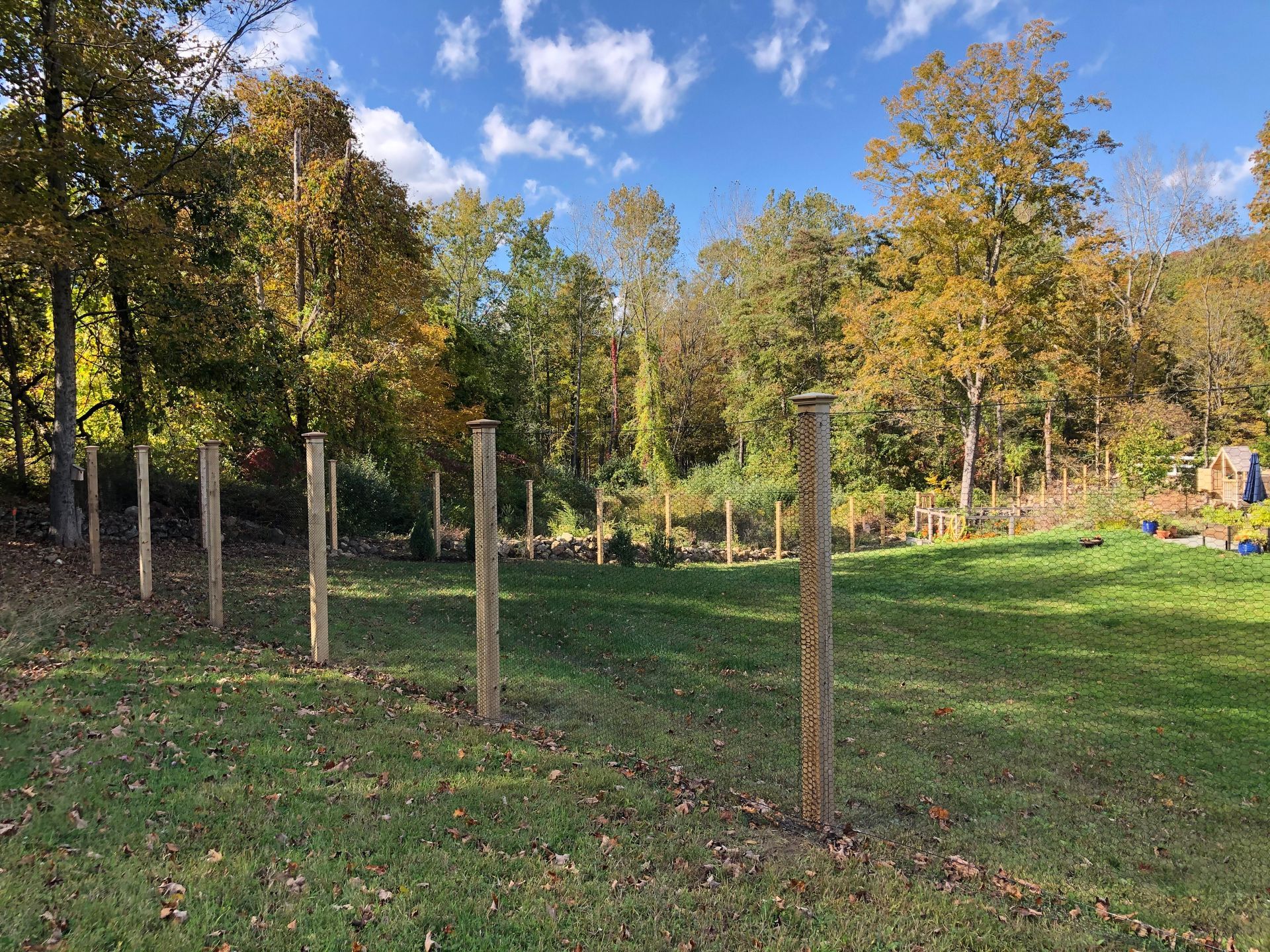 A wooden fence surrounds a grassy field with trees in the background.