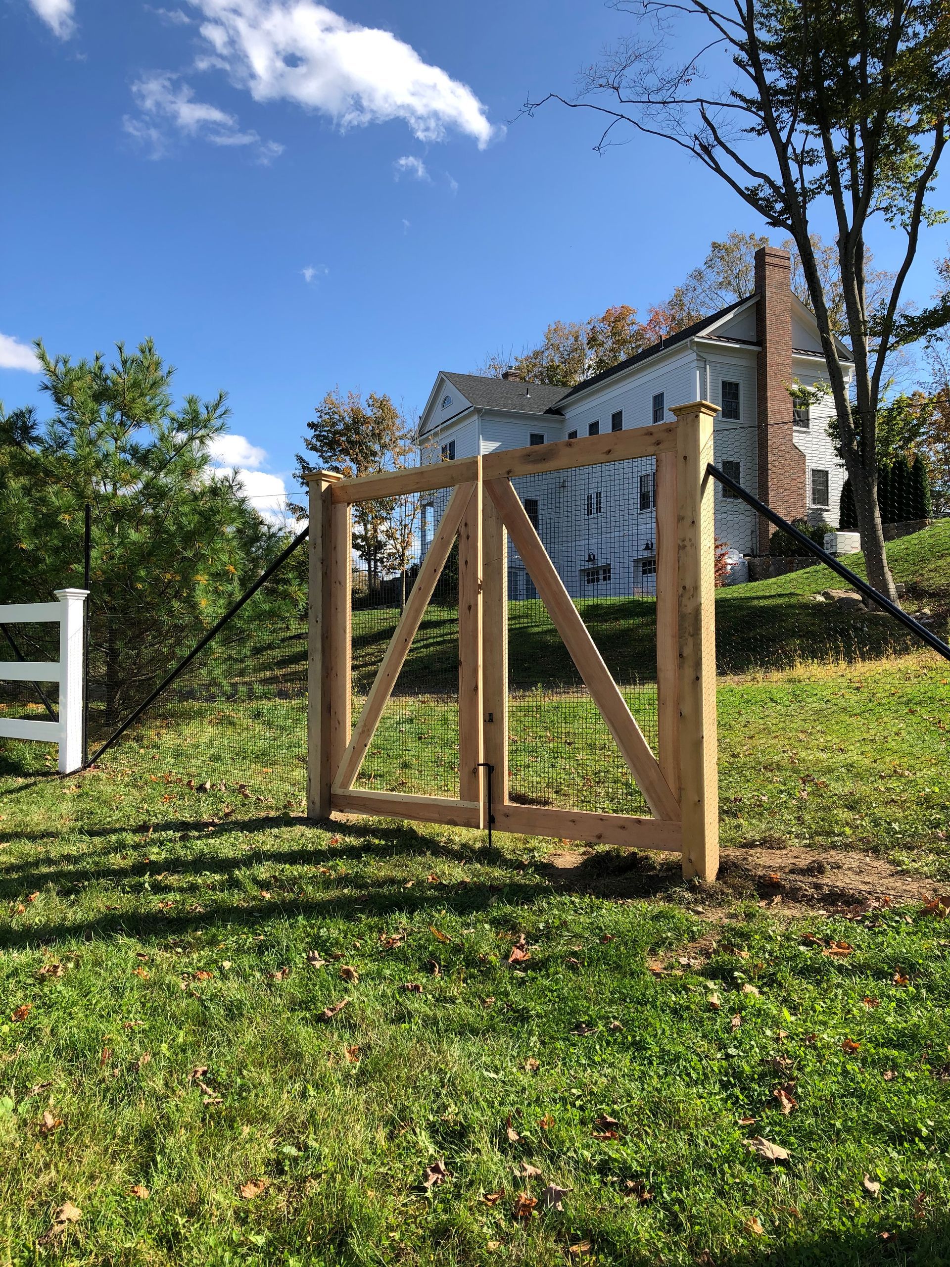 A wooden gate is in the middle of a grassy field in front of a house.