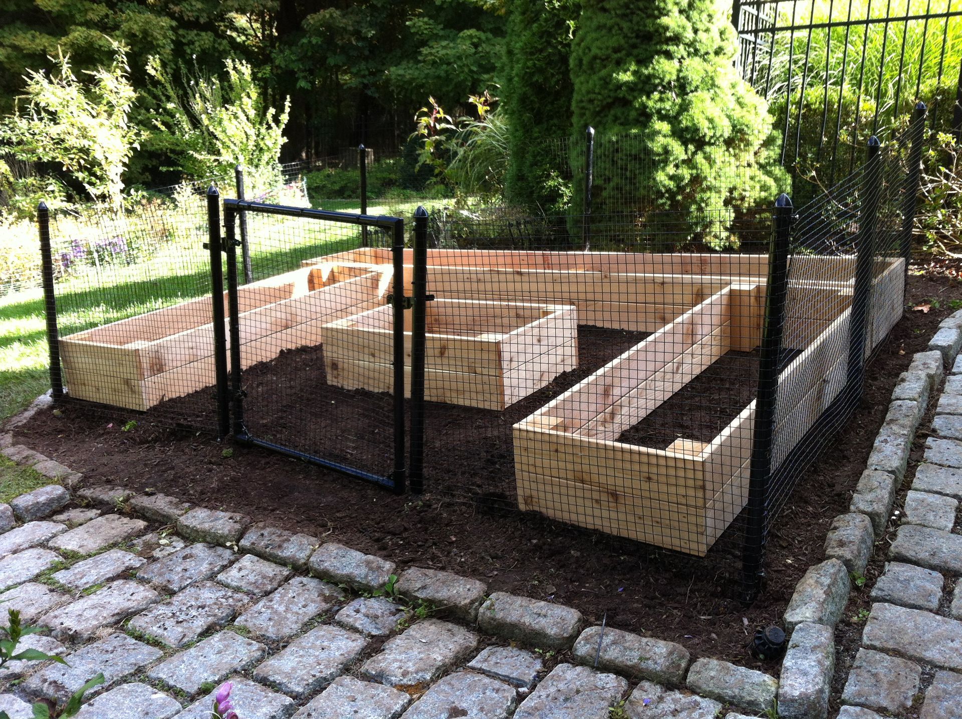 A garden with wooden raised beds and a gate surrounded by bricks.