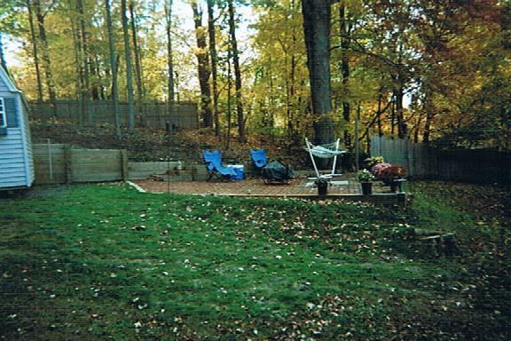 A backyard with a shed and chairs in the woods.