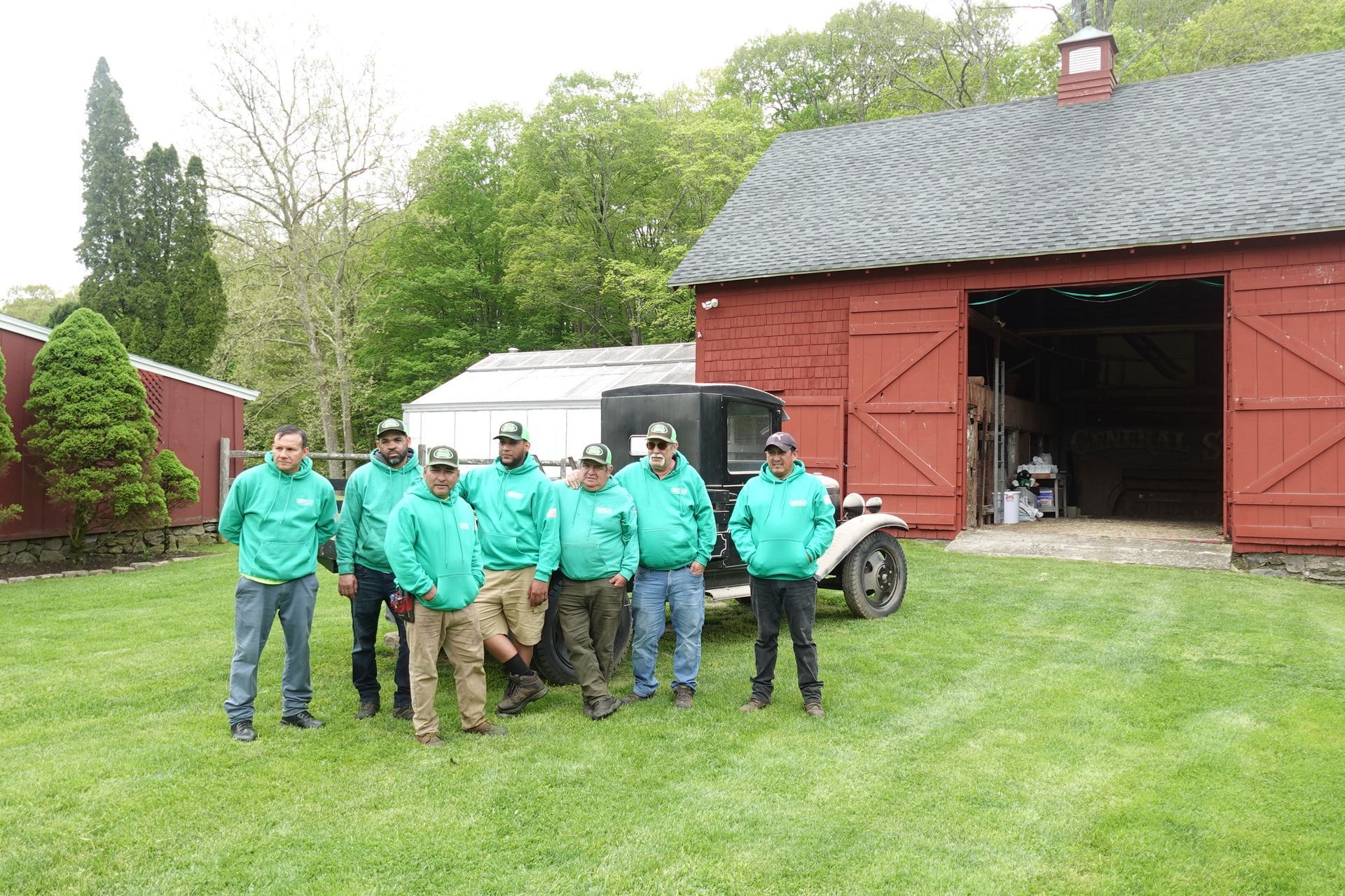 A group of men in green shirts are standing in front of a red barn