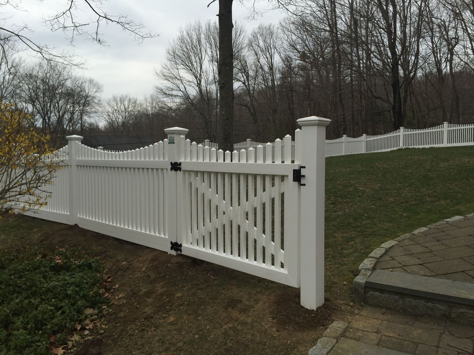 A white picket fence with a gate is surrounded by grass and trees.