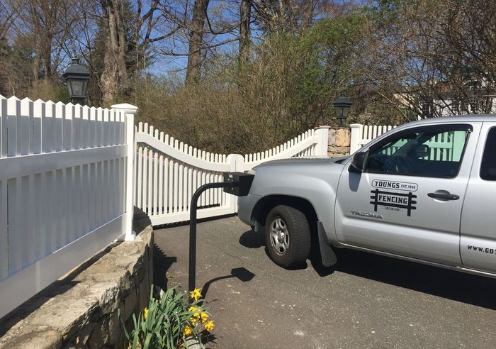 A silver truck is parked in front of a white picket fence.