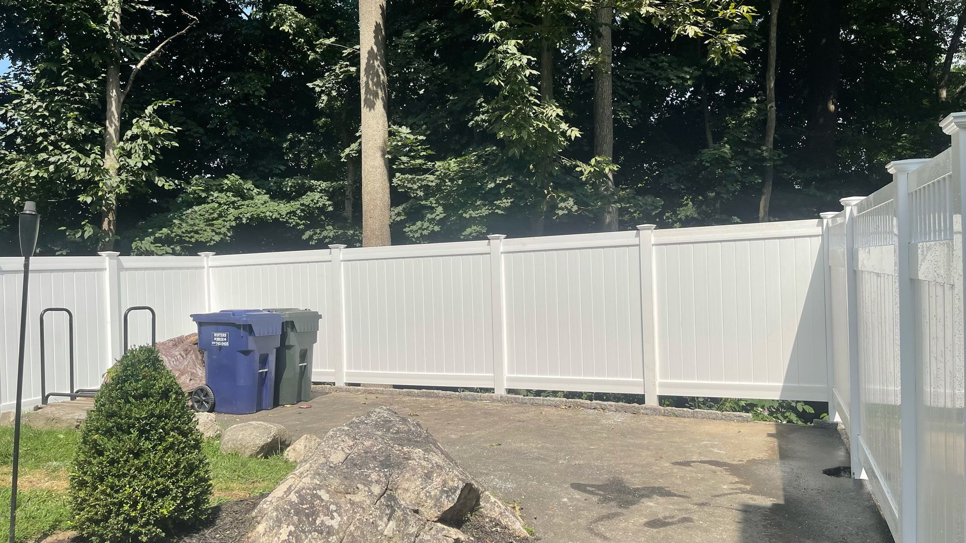A white fence with blue trash cans in front of it.