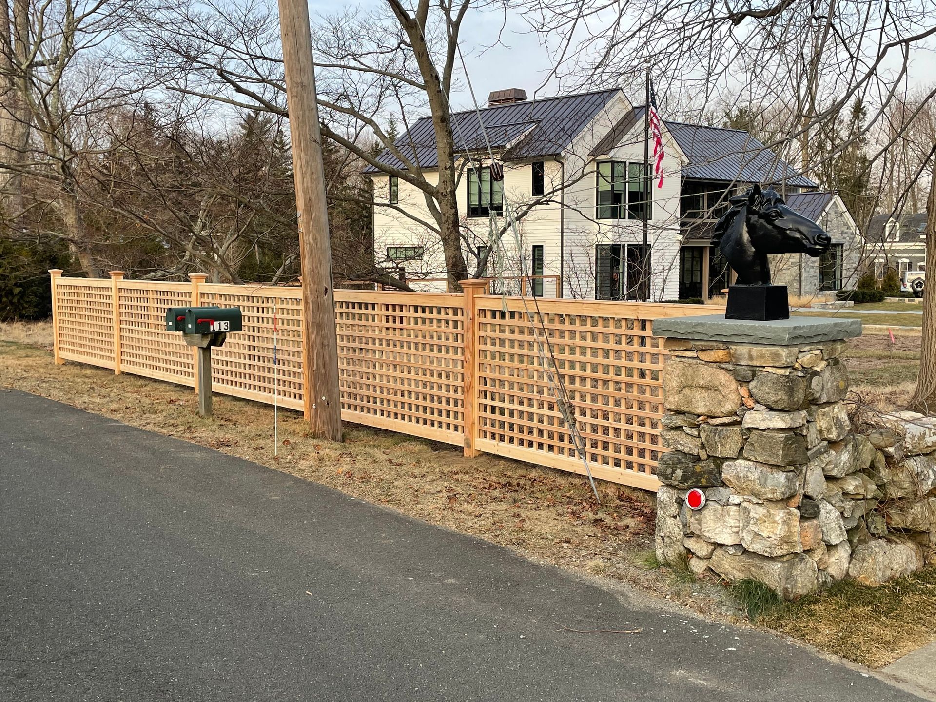 A wooden fence surrounds a stone wall in front of a large house.