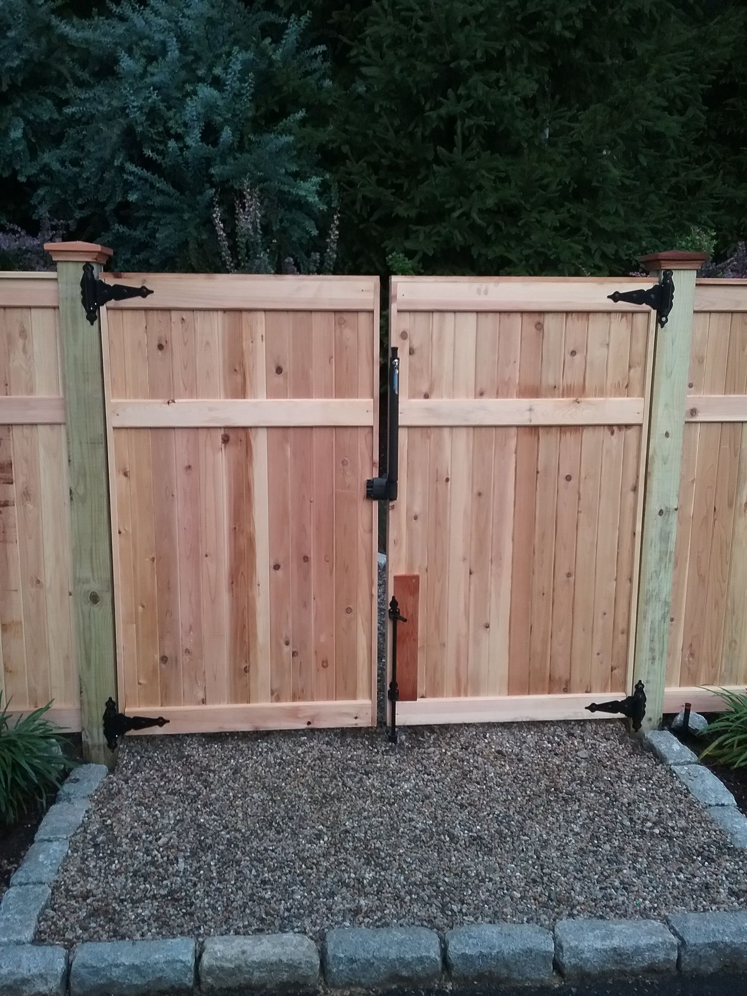 A wooden gate is sitting on top of gravel next to a wooden fence.