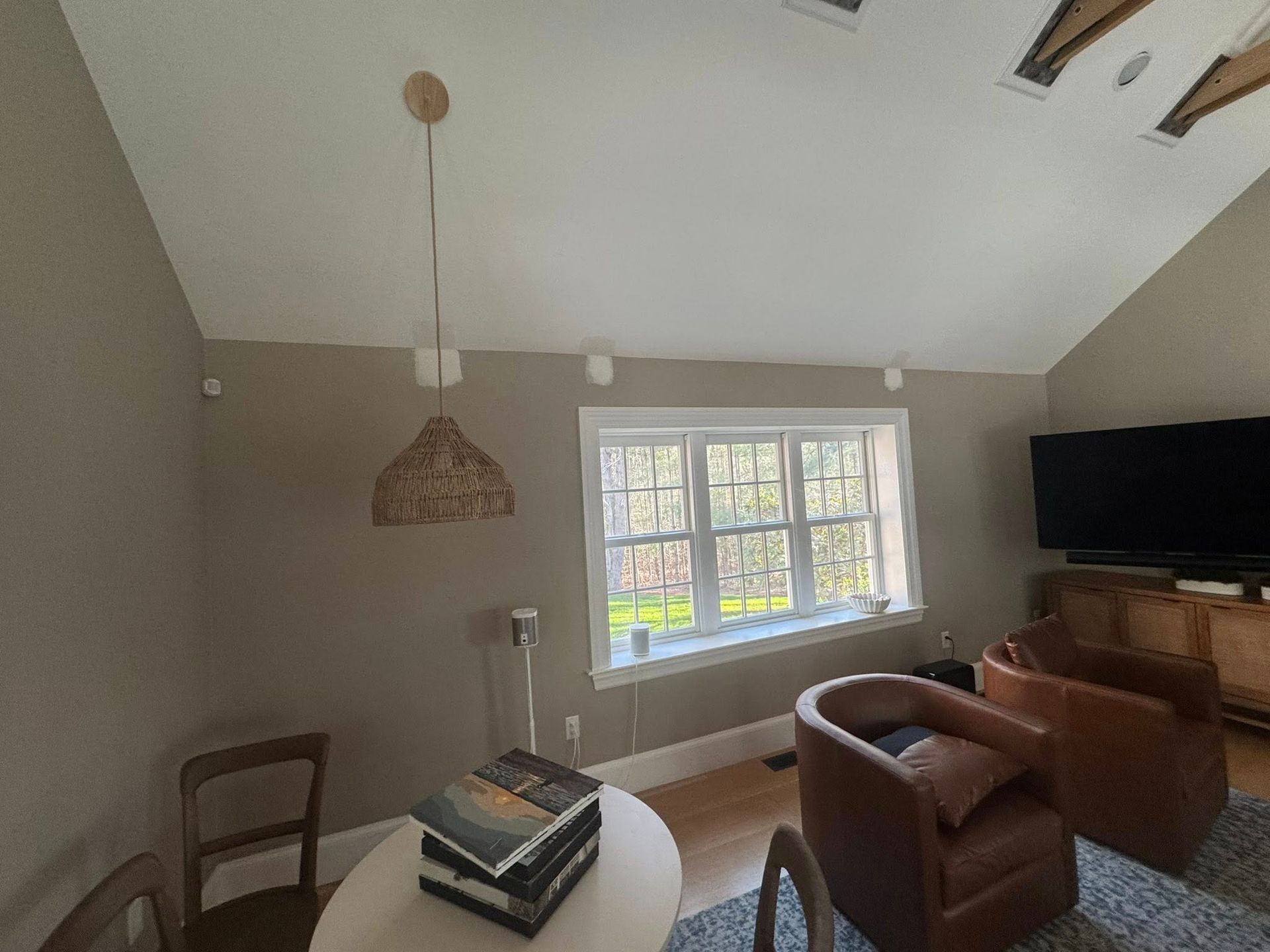 Cozy living room with a large window, brown chairs, a wall-mounted TV, and a woven pendant light.