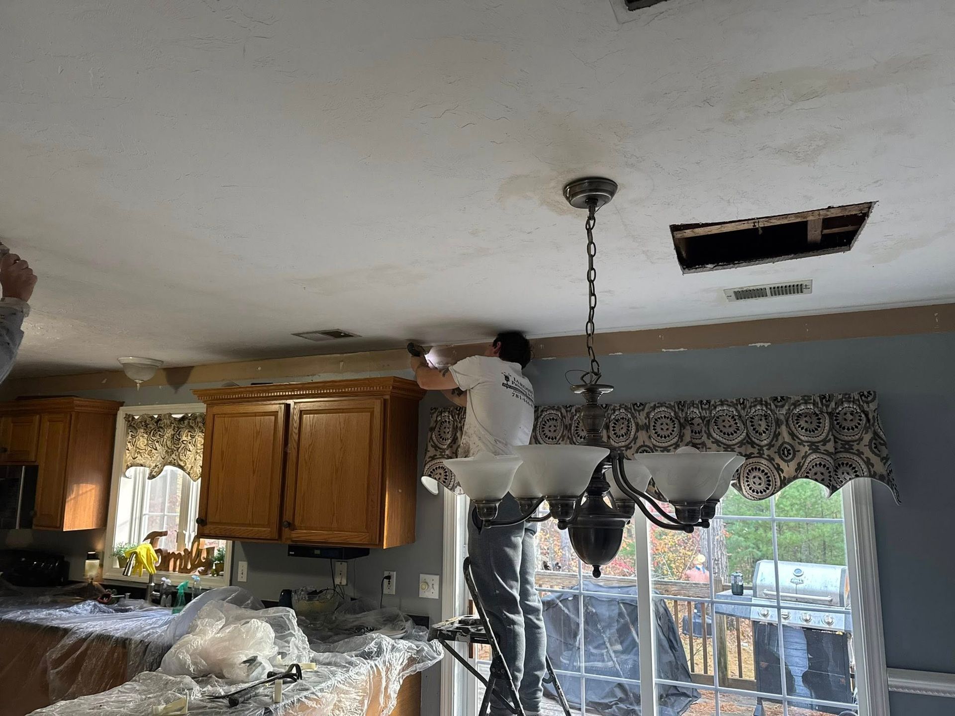 Person working on a kitchen ceiling next to a hanging light fixture and open vent hole