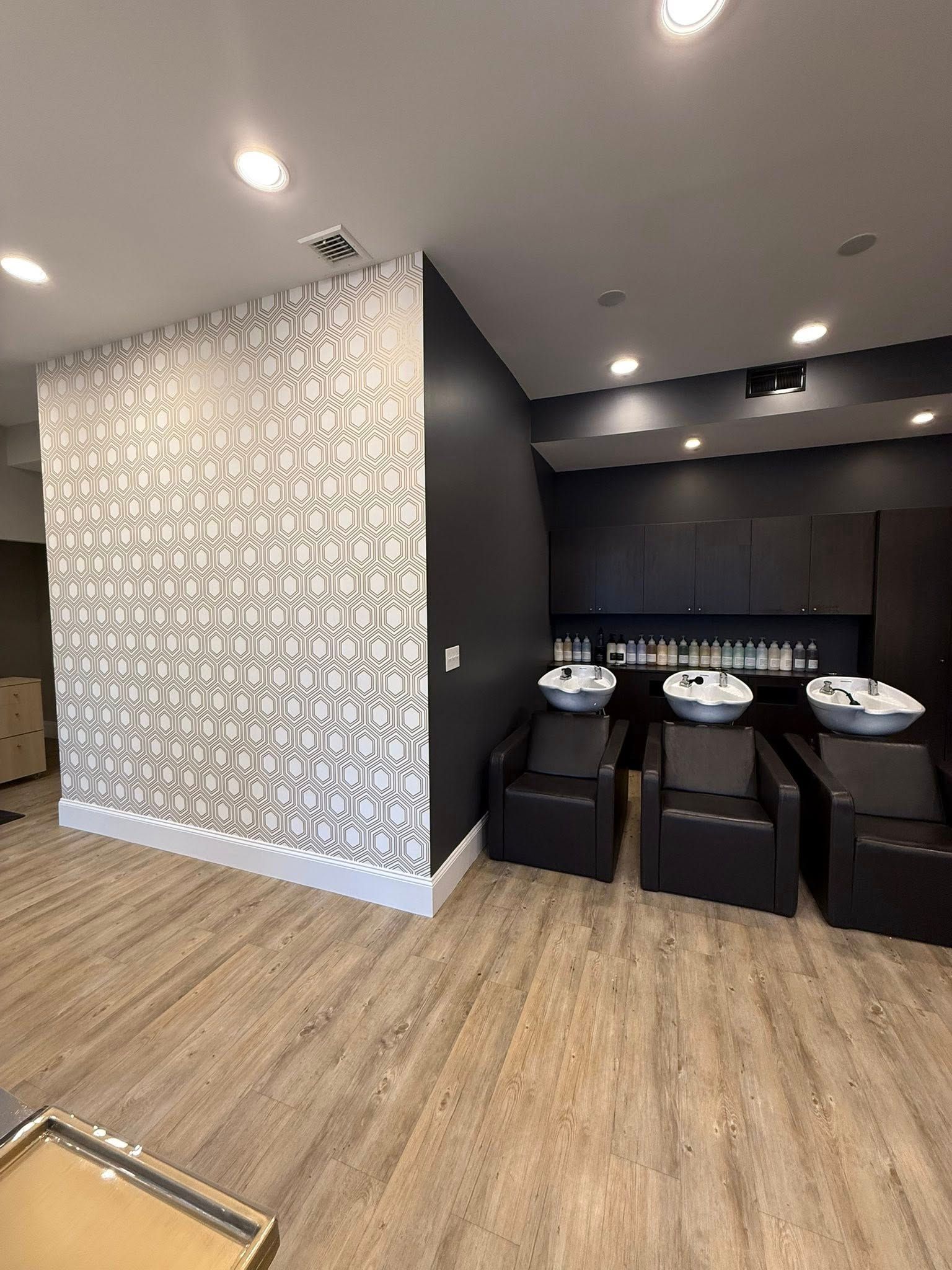 Modern salon with black wash basins, dark cabinetry, and wood flooring beneath recessed ceiling lights