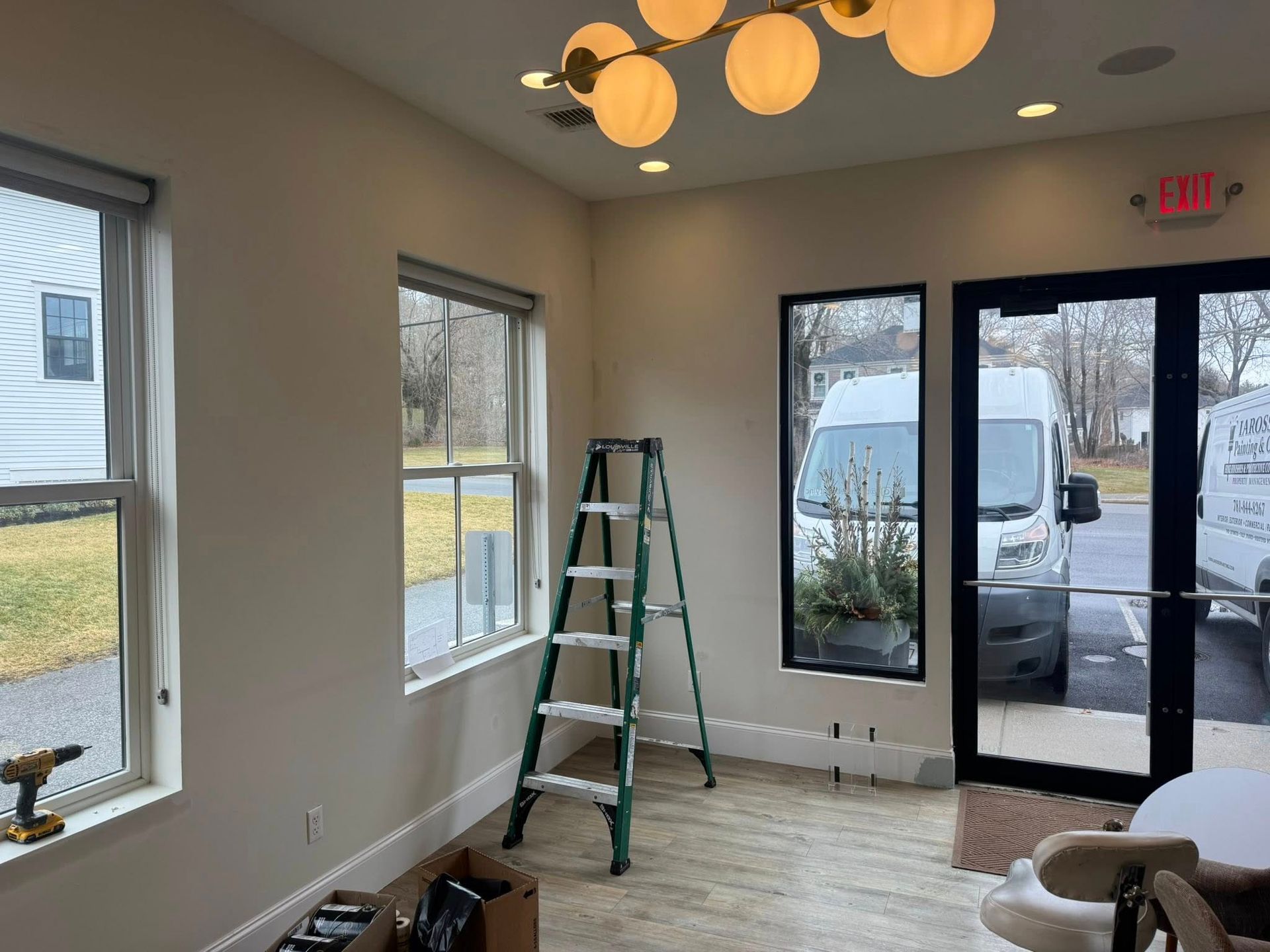 Interior room with windows, green ladder, and glass doors leading outside, under warm ceiling lights