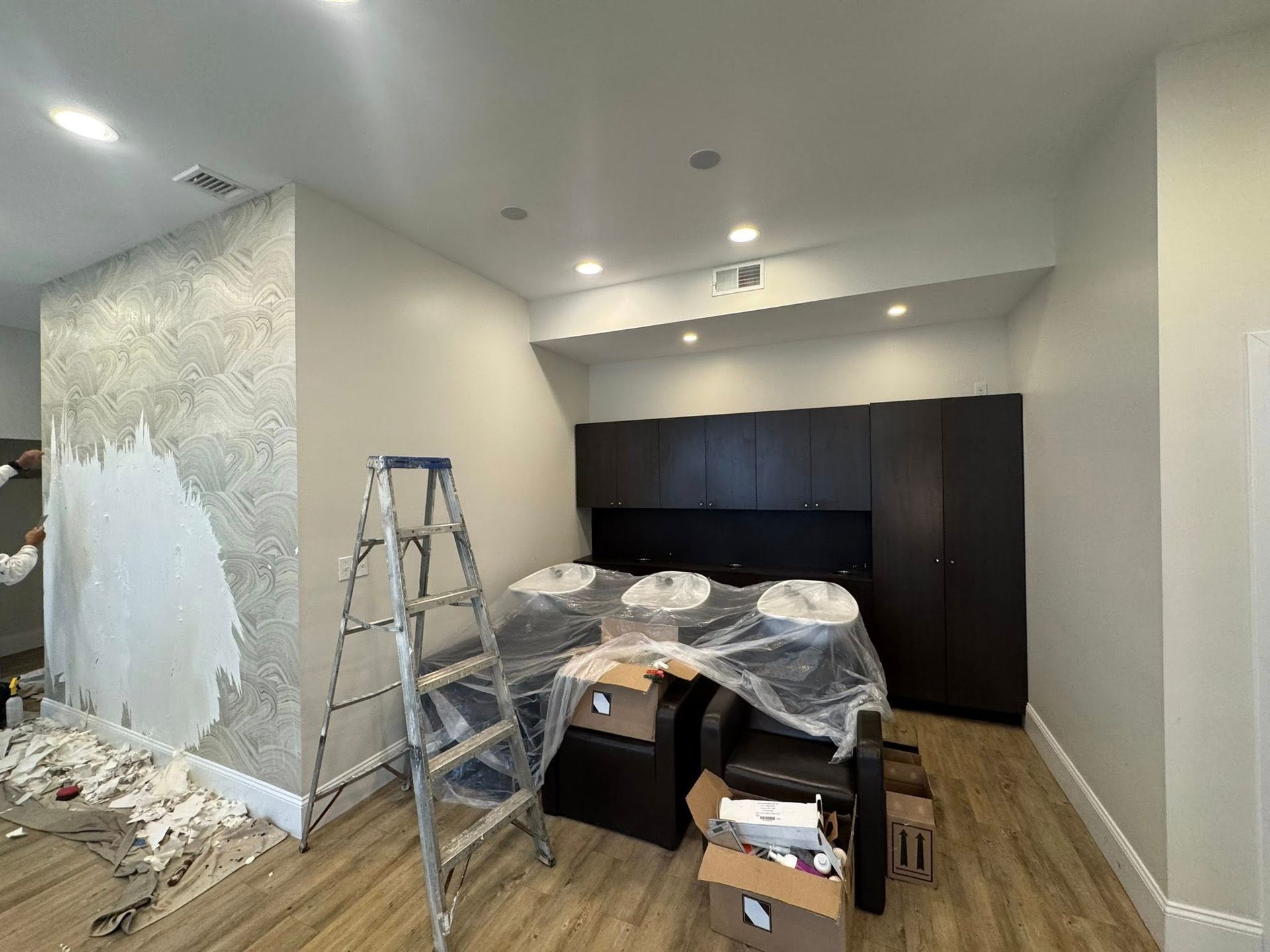 Partially renovated room with ladder, plastic-covered furniture, dark cabinets, and unfinished wall patches