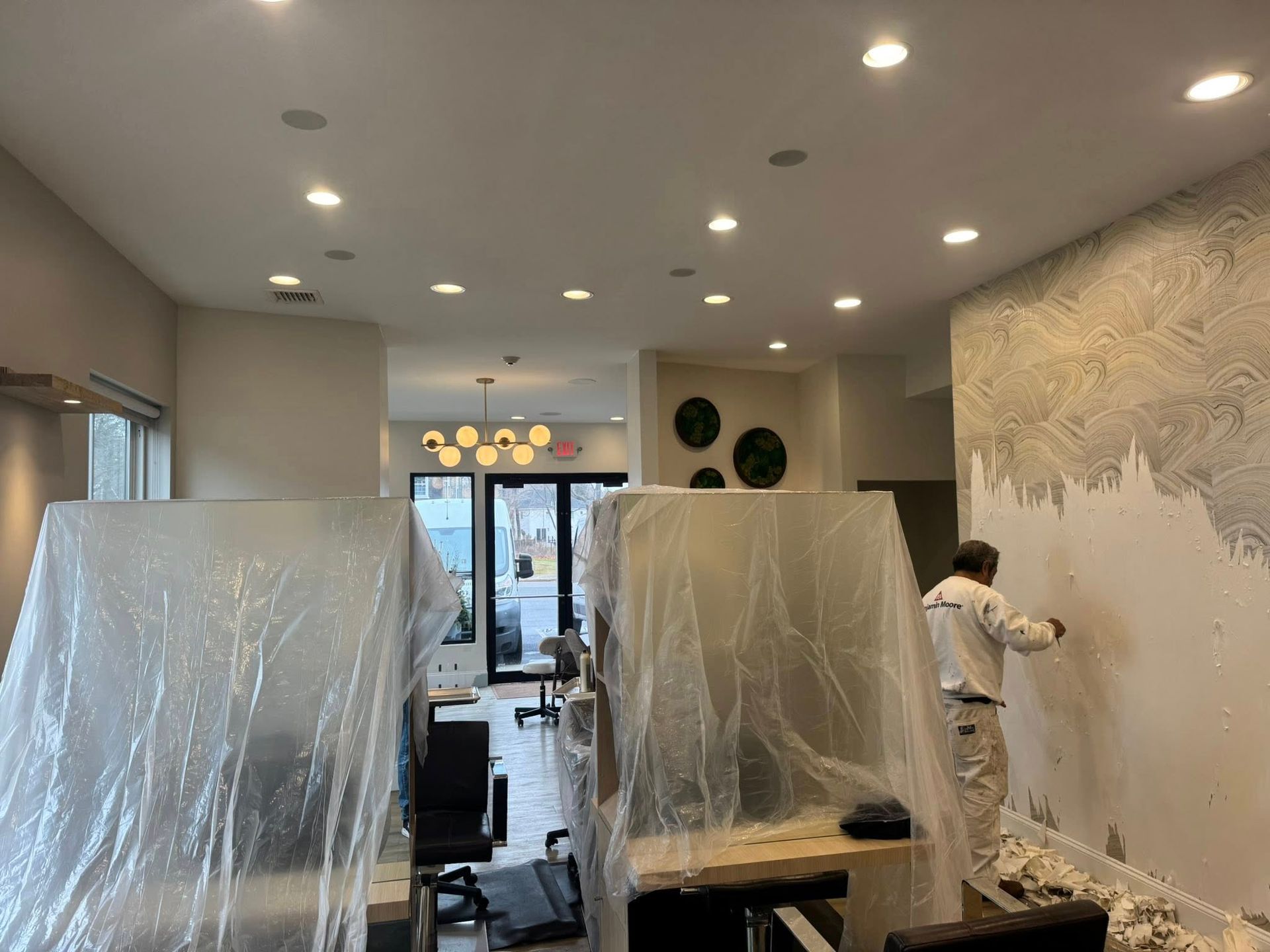 Partially renovated room with plastic-covered furniture and a person painting a mural on the wall