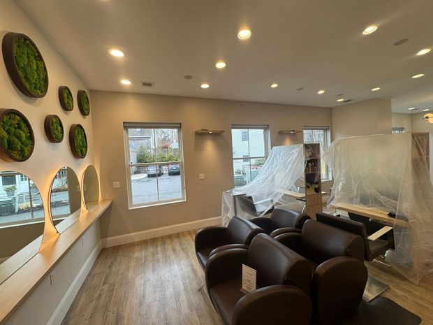 Modern salon interior with black chairs, wood floors, wall mirrors, and covered stations during renovation