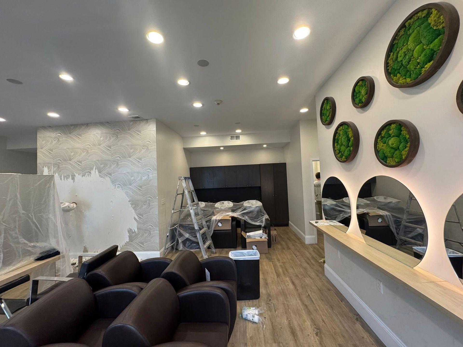 Modern hair salon interior with black chairs, mirrors, and green wall art under bright recessed lighting
