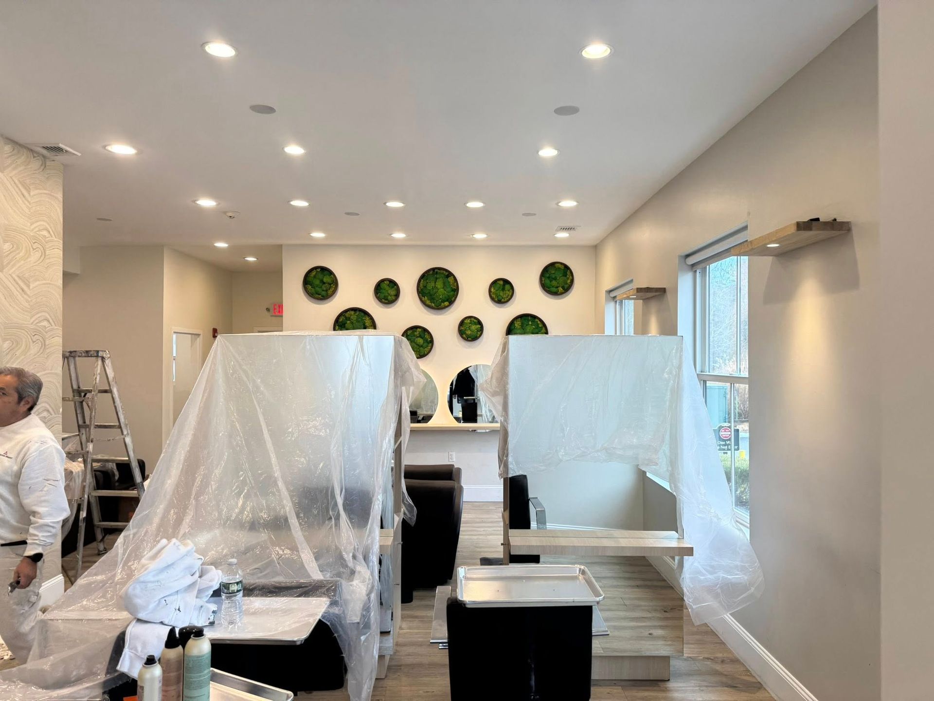 Interior of a room under renovation with plastic-covered furniture, ladders, and a green wall decoration.